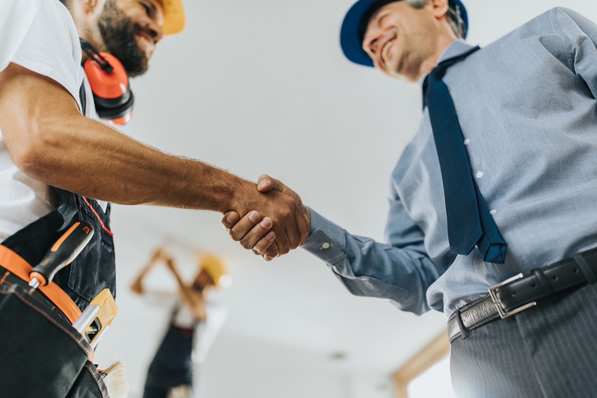 Below view of manual worker shaking hands with architect at construction site.