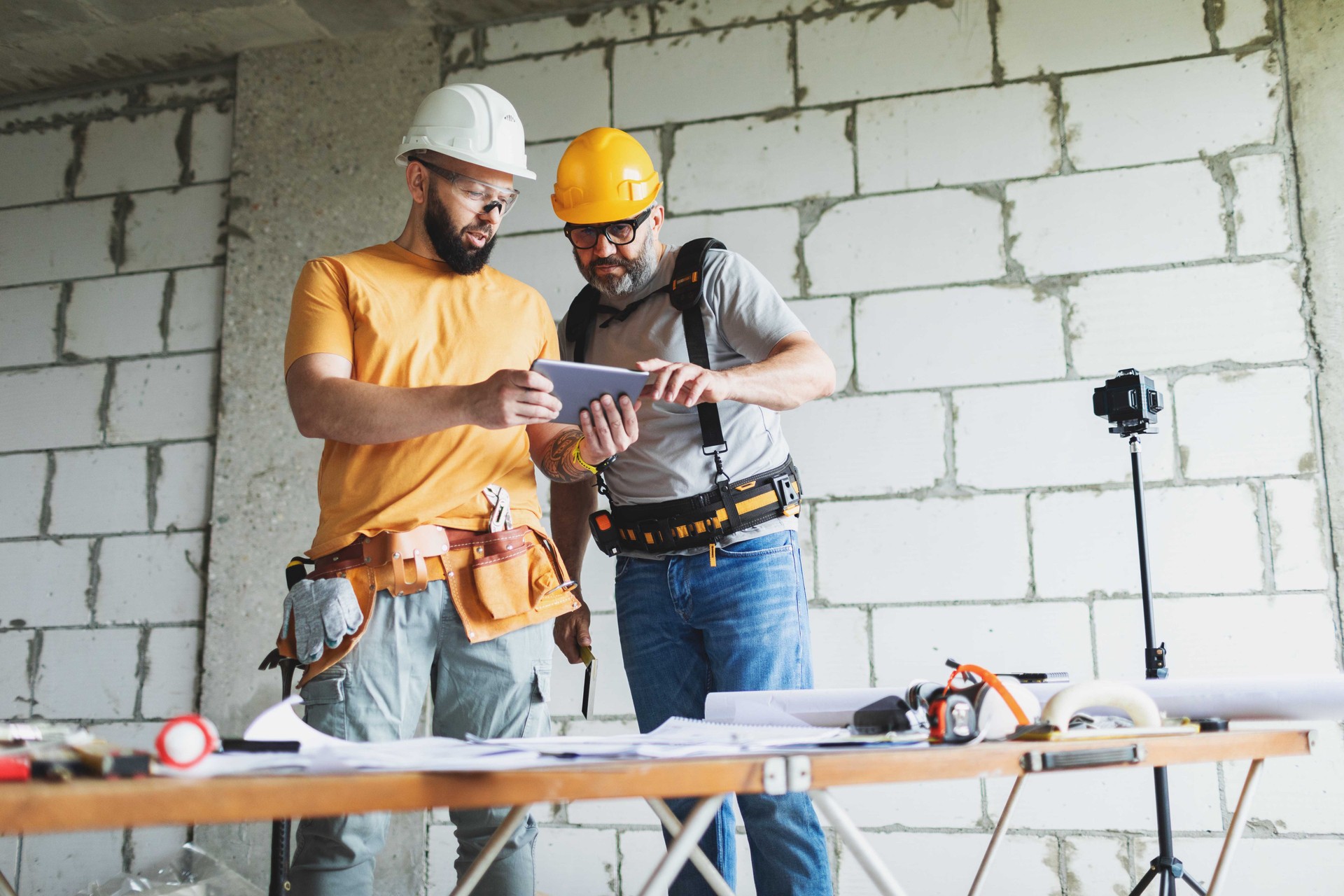 Low angle view of two construction workers analyzing blueprints using digital tablet at construction site